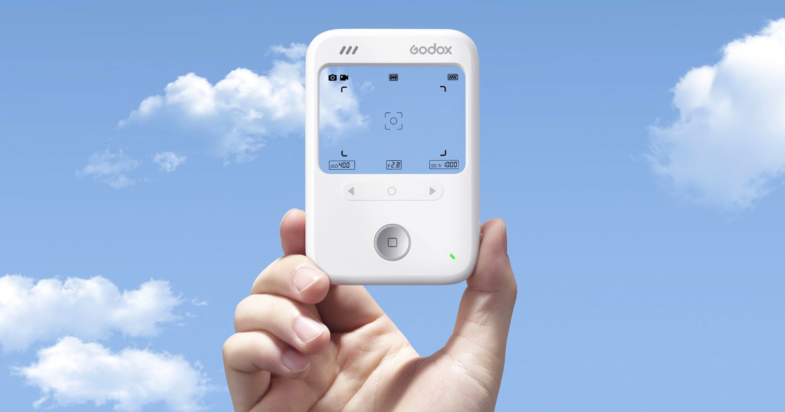 A hand holds up a white Godox electronic device with a screen displaying camera settings, against a blue sky with scattered white clouds.
