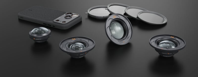 A smartphone with a textured case is surrounded by three detachable camera lenses and several circular lens filters on a dark surface, showcasing mobile photography accessories.