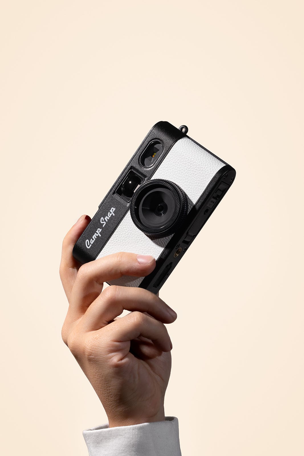 A hand holding up a black and white vintage-style film camera labeled "Camp Snap" against a plain, light beige background.