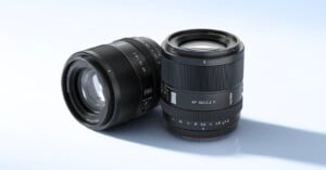 Two black camera lenses are displayed on a light blue surface, one standing upright and the other lying on its side. Both lenses have visible text and controls on their bodies.