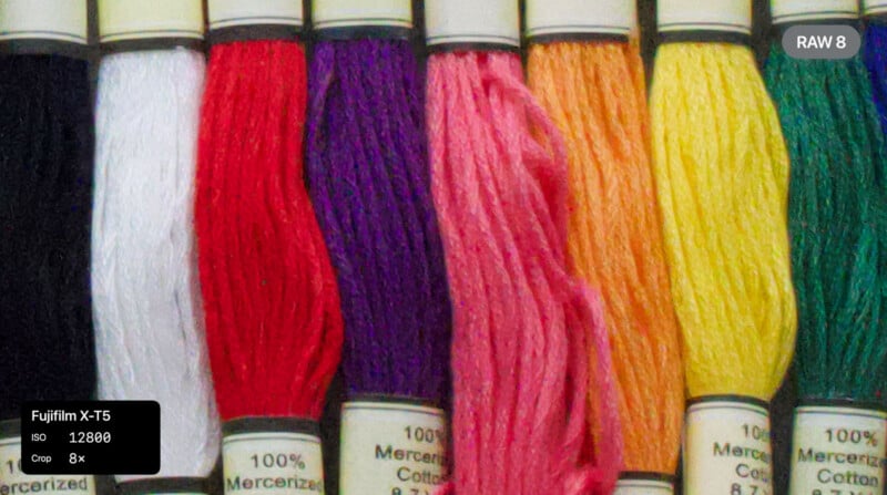 Close-up of eight skeins of embroidery thread in white, red, purple, pink, peach, yellow, orange, and beige, with camera settings overlaid in the corners. The image shows visible grain and texture from high ISO.