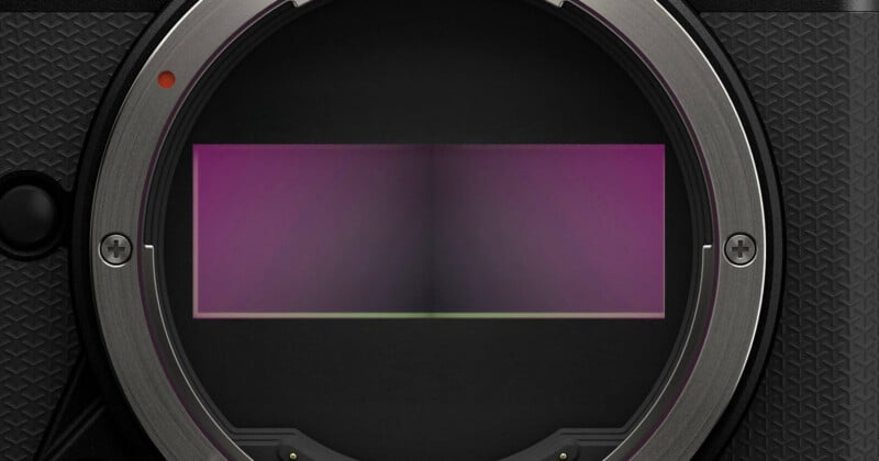 Close-up view of a digital camera's lens mount showing the exposed rectangular image sensor, which has a subtle purple and green gradient. The surrounding mount is metallic with small screws and textured grip.