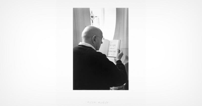Un hombre calvo con gafas lee un pequeño libro que dice "Piensa en ello" Escrito en una página abierta, junto a una ventana por la que entra luz.