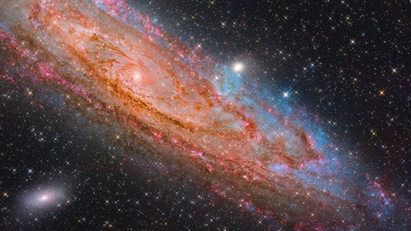 A vibrant, detailed image of the Andromeda galaxy shows swirling arms with pink, blue, and orange hues, surrounded by countless bright stars against the dark backdrop of space.