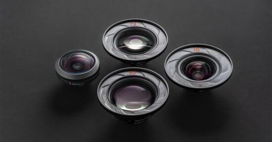 Four camera lenses of varying sizes are arranged on a dark surface. The lenses are labeled 21, 60, 75, and 100, with visible reflections on their glass elements.