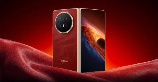 A luxurious smartphone with a red leather back and gold accents stands upright on a matching red surface. The screen displays a vivid space-themed wallpaper with a planet and glowing light. The brand "HONOR" is visible on the back.