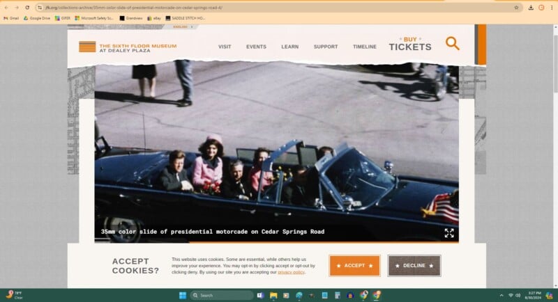 A historic color photo shows a presidential motorcade with several people in a dark convertible car driving down a street, with bystanders visible on the sidewalk and background.