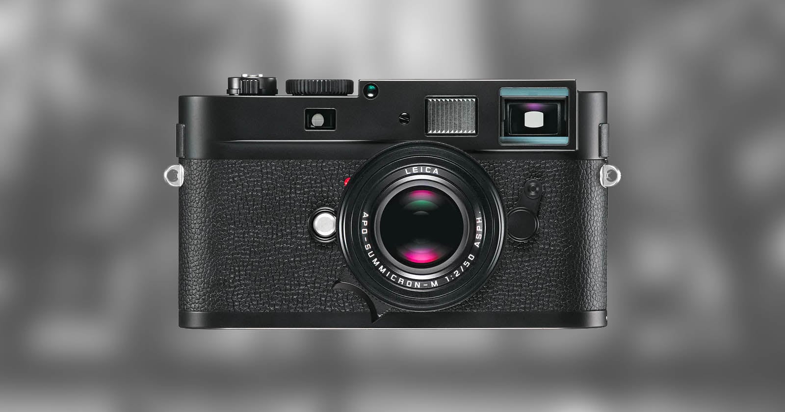 A black Leica digital camera with a textured grip, prominent lens, and various dials is centered against a blurred gray background.