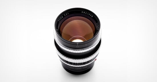 A camera lens with a black body and silver focus rings is shown from above on a white background. The glass elements reflect light, and text around the lens edge reads “TYPE Z1 LIGHT LENS LAB.”.