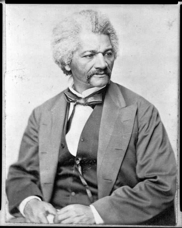 A Black man with gray hair and mustache, wearing a suit with a vest, bow tie, and white shirt, sits and looks to the side in this black-and-white historical portrait photograph.