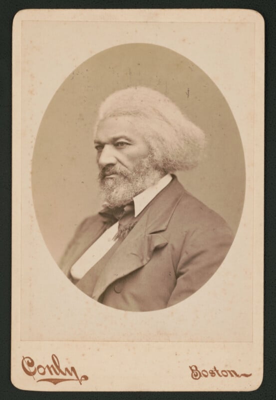 Sepia-toned portrait of an older man with white hair and beard, wearing a suit and bow tie, facing left. The photo is in an oval frame with “Conly” and “Boston” written below.