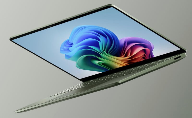 A sleek, partially open silver laptop is shown floating against a gray background, displaying a colorful Windows wallpaper on its screen.