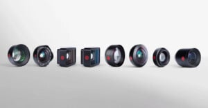A row of seven different camera lenses and lens attachments, each with distinct shapes and glass elements, displayed against a plain white background.