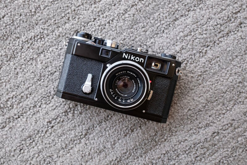 A vintage Nikon film camera with a textured black body sits on a light gray carpeted surface.