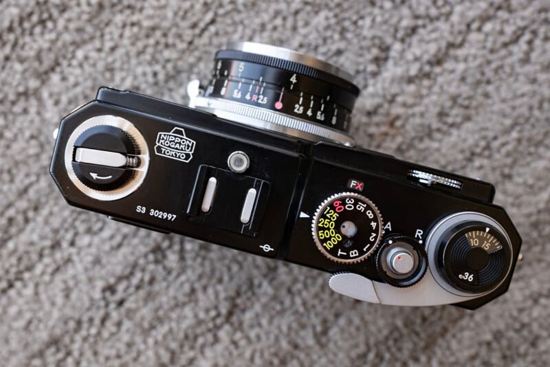 Top view of a vintage black film camera with various control dials, including shutter speed and ISO, and a lens showing aperture settings, placed on a textured gray carpet.