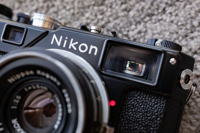 Close-up of a black Nikon camera showing the brand name, lens, and viewfinder details, with a textured background and light reflecting off the lens glass.
