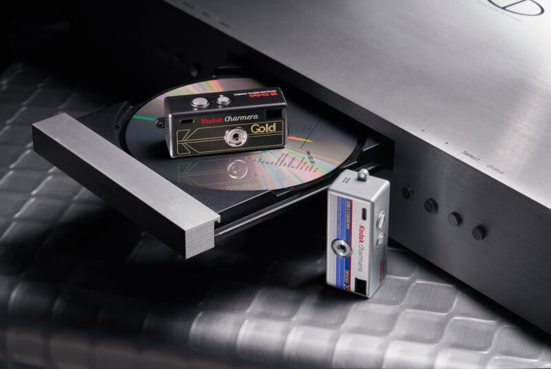 Two Kodak film canisters, one labeled "Gold" and the other "Color Plus," are placed on and beside the open tray of a silver CD player, with a CD partially out on the tray.