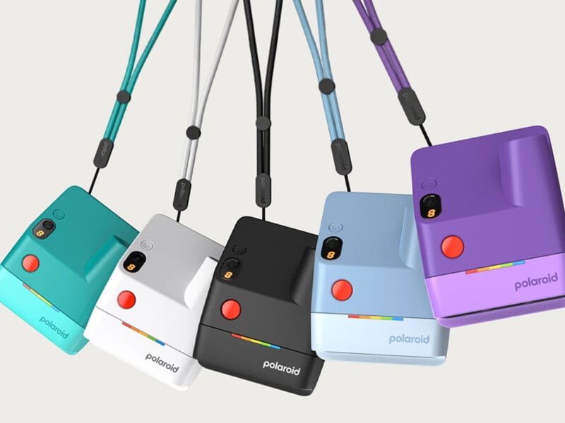 Five Polaroid instant cameras in teal, white, black, blue, and purple hang from matching straps, arranged in a row against a plain light background.