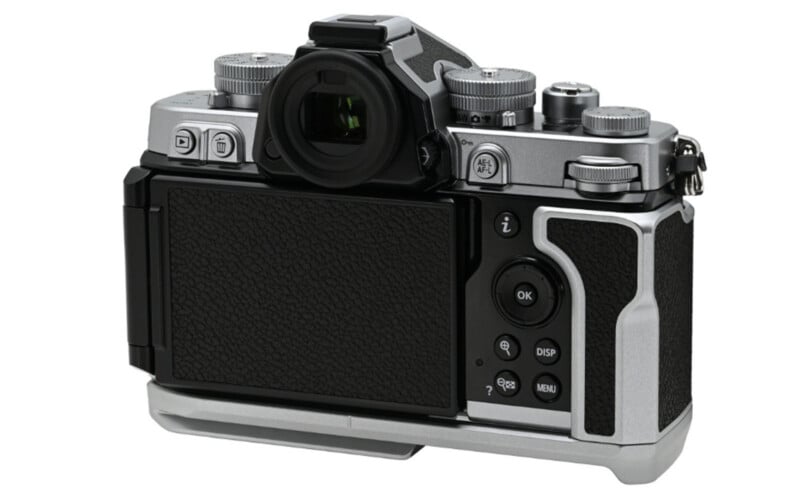 A silver and black digital camera is shown from the back, displaying its LCD screen, control buttons, viewfinder, and various dials, with a retro-style body design.