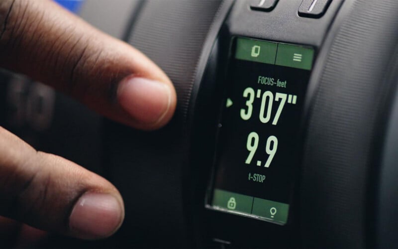 A close-up of a hand adjusting a camera lens with a digital display showing focus distance set to 3 feet 7 inches and the f-stop value at 9.9.