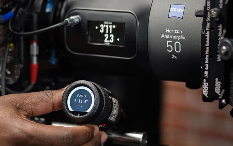 A close-up of a hand adjusting a focus control on a device, with a Zeiss Horizon Anamorphic 50mm camera lens and a digital focus display screen in the background.