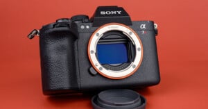 A Sony Alpha 7R mirrorless camera without a lens, showing the sensor and E-mount, placed on a red surface with the lens cap in front.