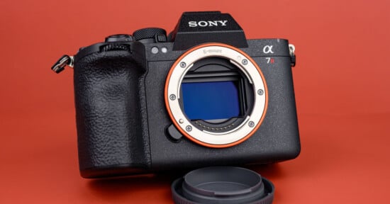 A Sony Alpha 7R mirrorless camera without a lens, showing the sensor and E-mount, placed on a red surface with the lens cap in front.