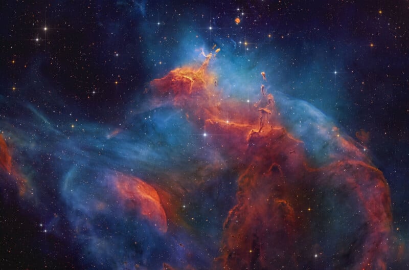 Colorful nebula in deep space featuring swirling clouds of blue, red, and orange gas and dust, illuminated by bright stars scattered across a dark background.