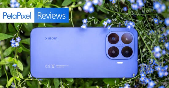 A blue Xiaomi smartphone with triple camera lenses lies among green leaves and small blue flowers. The image has a "PetaPixel Reviews" label in the top left corner.