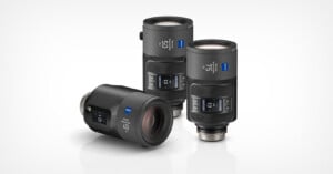 Three Zeiss camera lenses are displayed on a white background, two standing upright and one lying on its side, all featuring digital display screens and marked with focal lengths of 21, 35, and 50 millimeters.