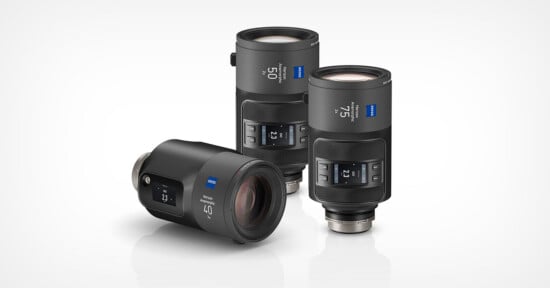 Three Zeiss camera lenses are displayed on a white background, two standing upright and one lying on its side, all featuring digital display screens and marked with focal lengths of 21, 35, and 50 millimeters.