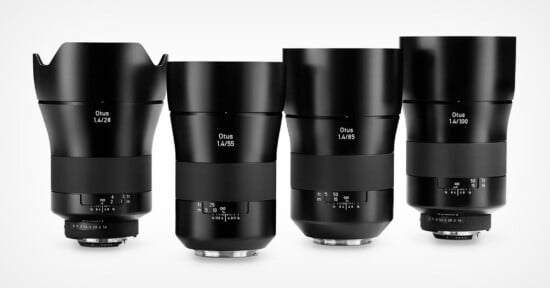 Four black Zeiss Otus camera lenses of different focal lengths (28mm, 55mm, 85mm, and 100mm) are standing upright in a row on a white background.