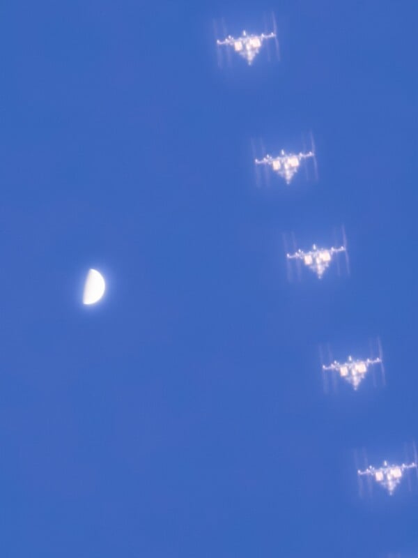 Secuencia de la Estación Espacial Internacional pasando por la media luna bajo un cielo azul claro, tomada a través de múltiples exposiciones para mostrar su movimiento.