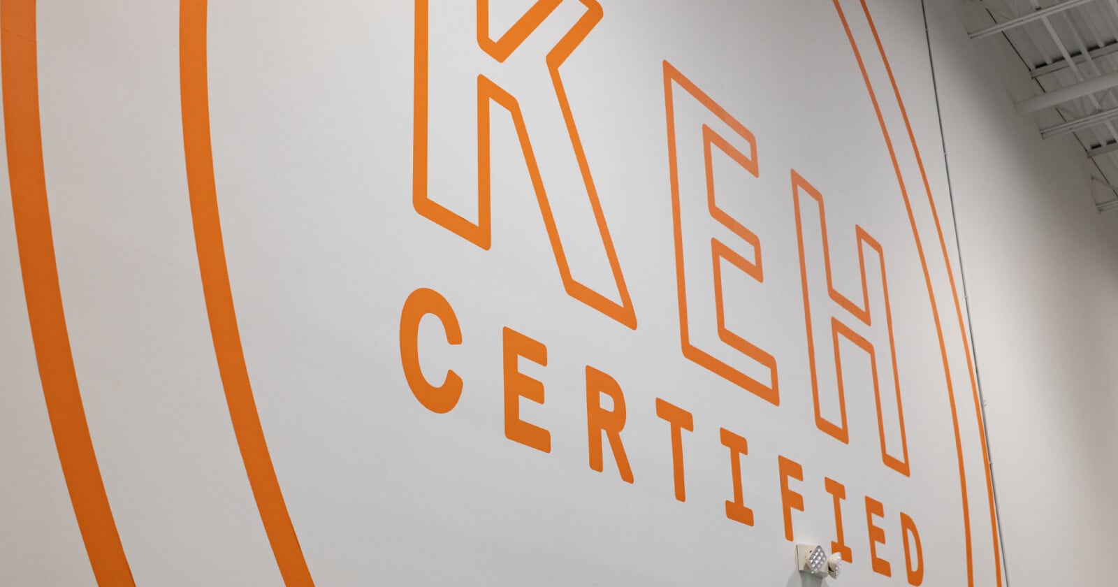 A large orange logo reading "KEH CERTIFIED" is painted on a white wall, framed by two concentric orange circles.