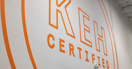 A large orange logo reading "KEH CERTIFIED" is painted on a white wall, framed by two concentric orange circles.