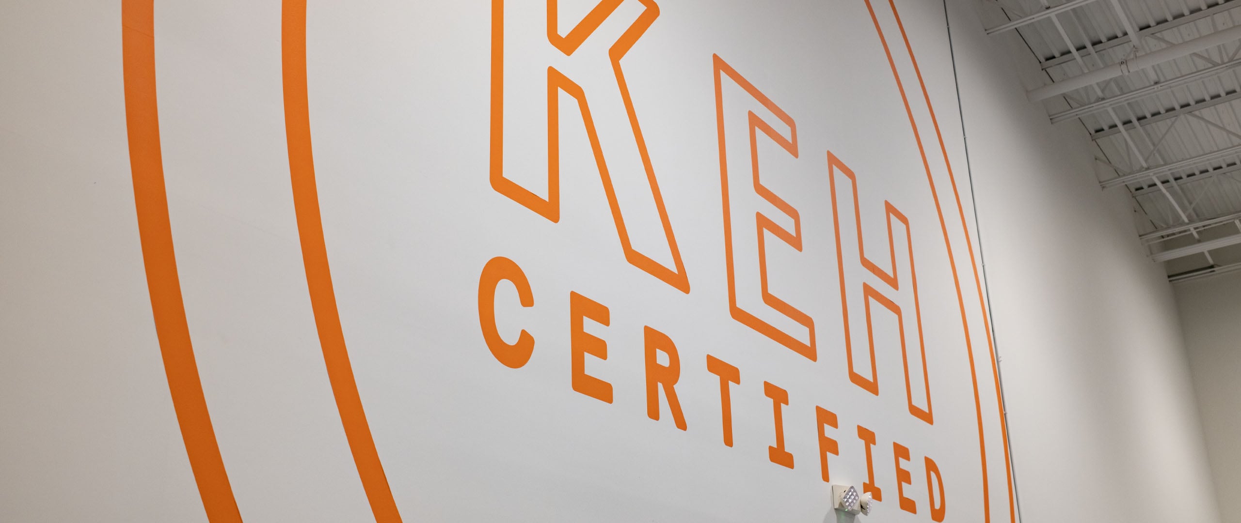 A large orange logo reading "KEH CERTIFIED" is painted on a white wall, framed by two concentric orange circles.