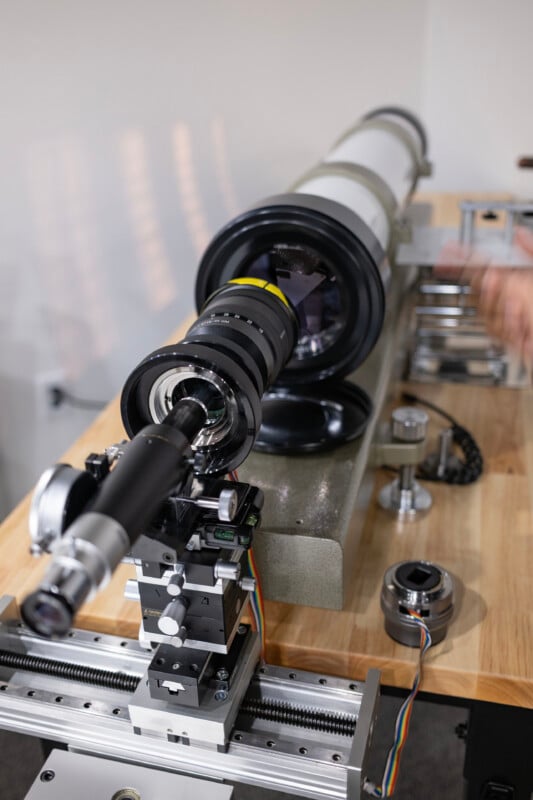 A camera lens is mounted on a precision optical bench, with a smaller eyepiece assembly positioned on a sliding rail in front of it.