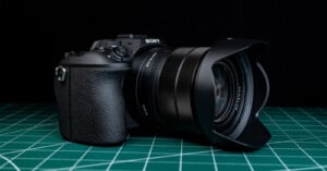 A black Sony digital camera with a wide lens hood is placed on a green cutting mat with grid lines. The background is solid black.