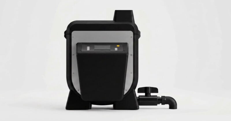 A black and silver industrial device with a digital display, control buttons, and a black pipe fitting with a valve on the right side, set against a white background.