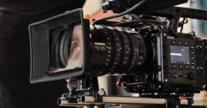 A close-up of a professional video camera with a large lens and various control dials, mounted on a tripod, ready for filming.