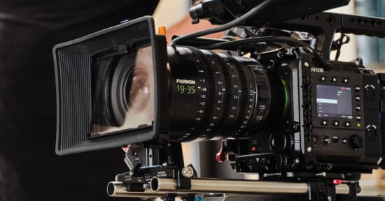 A close-up of a professional video camera with a large lens and various control dials, mounted on a tripod, ready for filming.