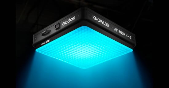 A square Godox KNOWLED AM1800R LED light panel emits a bright blue glow downward, illuminating the area below in a dark environment.