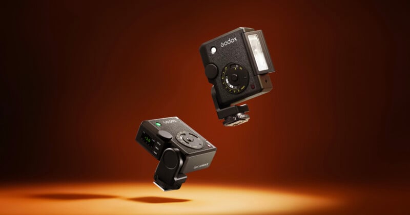 Two black compact cameras with flash attachments are suspended against a brown gradient background, with a spotlight below, giving a floating appearance.