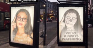 Two bus stop ads show a woman in glasses; the left ad is normal, the right is defaced with skull makeup and "Meta WE'RE ALWAYS WATCHING" written on it. The street and buildings are visible in the background.