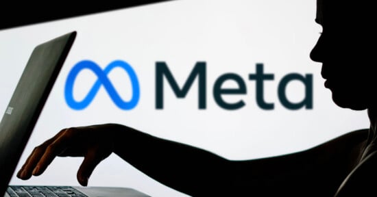 A silhouette of a person using a laptop in front of a screen displaying the Meta logo and name on a white background.