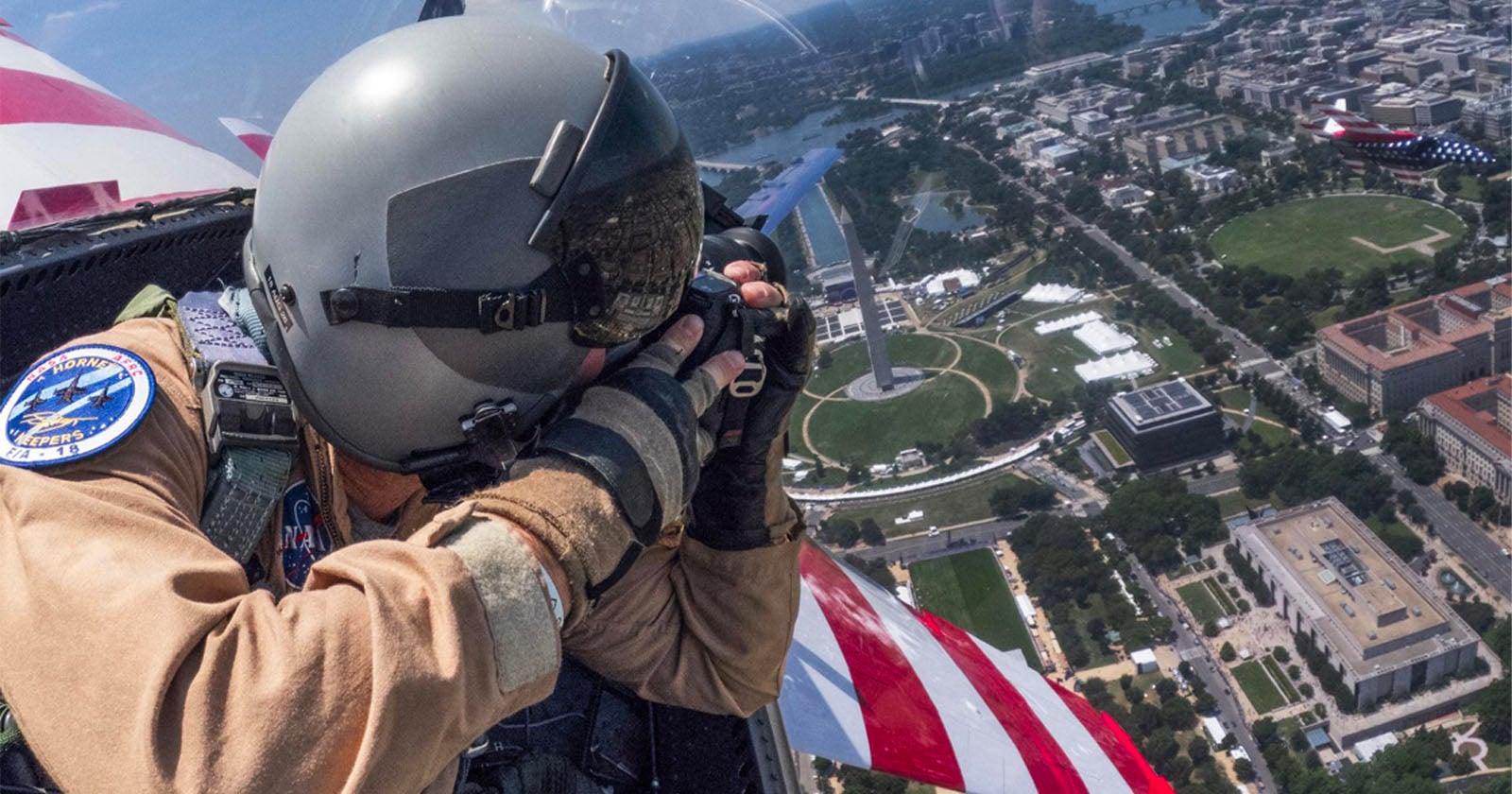 A pilot in a helmet takes a photo from a cockpit above Washington, D.C., with the Washington Monument and cityscape visible below.