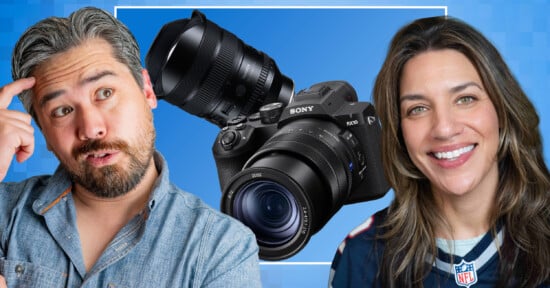 A man and a woman are smiling in front of a large Sony camera on a blue background. The man looks puzzled, touching his temple, while the woman smiles warmly, wearing a dark sports jersey.