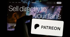 A hand holds a phone displaying the Patreon logo in front of a screen with the text "Sell directly to your fans.