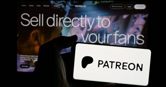 A hand holds a phone displaying the Patreon logo in front of a screen with the text "Sell directly to your fans.