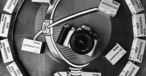 A Nikon camera sits in the center of a circular graphic surrounded by several boxes of Rollei Superpan 200 film.